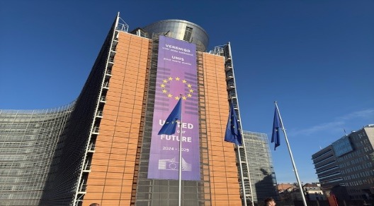 Questa fotografia mostra il Berlaymont, l'edificio sede della Commissione Europea a Bruxelles, Belgio. Il grande striscione blu al centro dell'edificio presenta il simbolo dell'Unione Europea (le 12 stelle dorate su sfondo blu) e lo slogan "United for our Future" (Uniti per il nostro futuro) per il periodo 2024-2029. Le lingue utilizzate (olandese, francese e inglese) sono le lingue ufficiali del Belgio e dell'UE.  L'immagine rappresenta un simbolo dell'Unione Europea e delle sue istituzioni, evidenziando un messaggio di unità e cooperazione per il futuro dell'Europa.